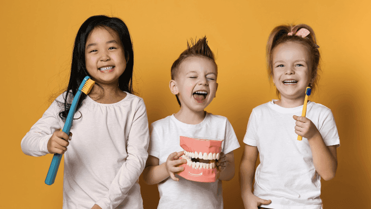 Three young kids holding a toothbrush and tooth model